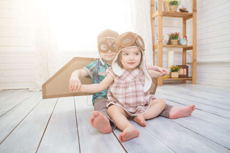 Happy children playing with vintage wooden airplane. Kids having fun at home. Imagination and freedom concept. Two little children wearing pilot costume and playing with old suitcaseの写真素材