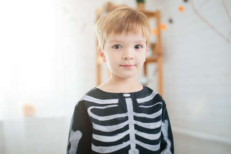 Holiday halloween. Funny little boy in a skeleton costume is ready to celebrate Halloween. Boy in a halloween dress-up room.の写真素材