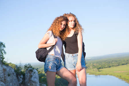 A world without borders. Stunning journey of two girls in the mountains. Two friends hugging looking at the mountains. Two girls on top of the mountain watching at sunset.の写真素材