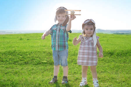 Brother and sister in suits of pilots are walking in field. Start traveling from childhood even in imagination. Teacher helping young boy with writing lesson. Back to school concept.の写真素材