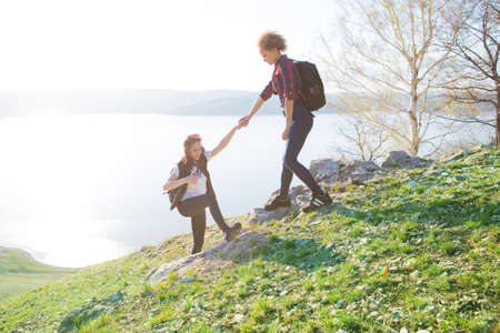 Two girls hikers climbing up mountain cliff and one of them giving helping hand. People helping and, team work concept.の写真素材