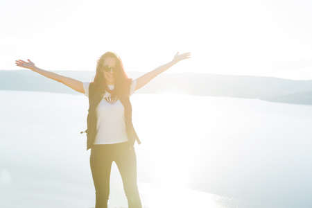 Beautiful girl Trist on top of a mountain on a background of sunset and sea. Happy hiker with her arms outstretched, freedom and happiness, achievement in mountainsの写真素材