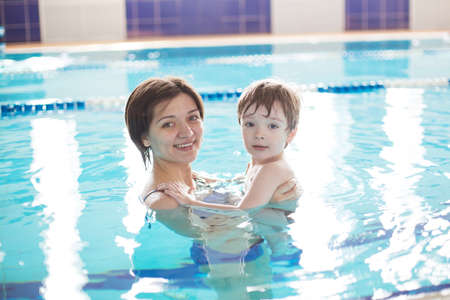 Young mother and her son having fun in a swimming pool. Healthy family mother teaching baby swimming poolの写真素材