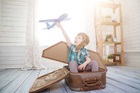 Little boy sits on a suitcase playing with model airplane. Fantasy travel concept.の写真素材