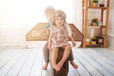 Happy children playing with vintage wooden airplane. Kids having fun at home. Imagination and freedom concept. Two little children wearing pilot costume and playing with old suitcase.の写真素材