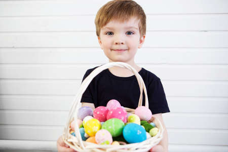 Happy baby boy with a basket of easter eggs on wooden background.の写真素材
