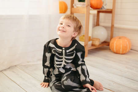Little cute boy in a skeleton costume is ready for the celebration of Halloween in the room with the scenery for Halloweenの写真素材