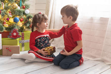 Boy gives a Christmas present to a girl in a bright sunny roomの写真素材