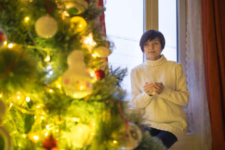 Happy young woman with cup of coffee or tea at home over christmas treeの写真素材
