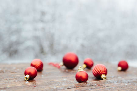 Beautiful Christmas bauble decorations lie on the wooden table over snow covered forest background.の写真素材