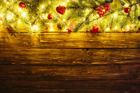Blurred Christmas background, with fir branches, fairy lights and christmas decorations on wooden plankの写真素材