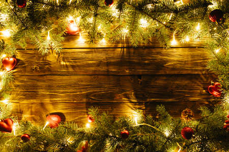 Border art design with Christmas tree, baubles and light garland Blurred Christmas background, with fir branches, fairy lights and christmas decorations on brown wooden plankの写真素材
