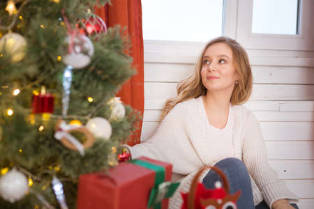 Beautiful, young woman decorating a Christmas tree at homeの写真素材