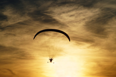 Paragliding at sunset. Silhouette against a background a cloudy sky colors the sunset.