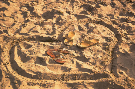 heart drawn on beach sand with male and female bedroom-slippes inside no people