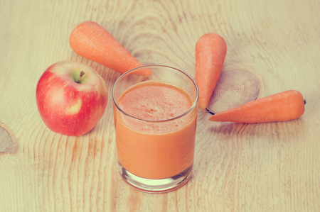 Retro filtered glass of freshly squeezed homemade mixed juice, apple and carrot on rustic wooden boardの写真素材