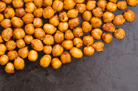 Chickpeas baked with spices closeup scattered on black metal background with place for textの写真素材