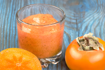 Glass of persimmon smoothie and ripe fruits on blue rustic wooden boardの写真素材