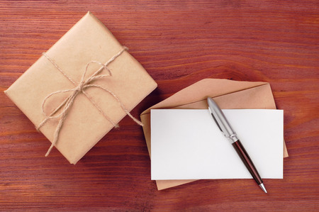 Rustic gift box and envelope with blank paper sheet and pen on wooden tableの写真素材