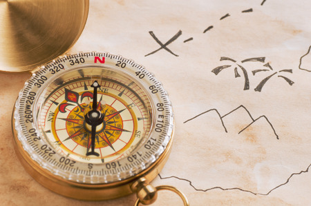 Closeup of compass over stained yellowed paper sheet with part of schematic hand drawn treasure mapの写真素材