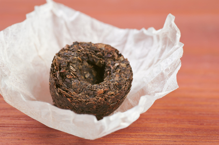 Unpacked dry pressed pu erh tea leaves briquette closeup on red wooden table, shallow depth of fieldの写真素材