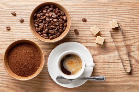 Coffee beans, ground coffee and cup of brewed coffee on rustic wooden table with sugar tongs, cane sugar cubes and coffee beans, view from aboveの写真素材