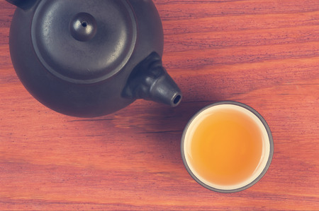 Clay glazed bowl with brewed tea and clay teapot on red wooden table top view with space for text, vintage filteredの写真素材