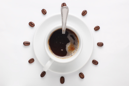 Coffee cup with spoon on saucer and coffee beans against white background forming clock dial viewed from above as symbol of morning, energy and cheerfulnessの写真素材