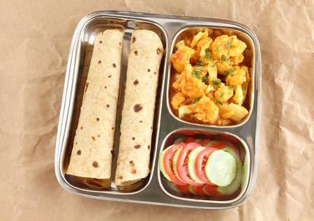 Chapati, also known as Indian flat Bread, with cauliflower curry as a side dish and slices of cucumber and tomato, in a steel plate.の写真素材