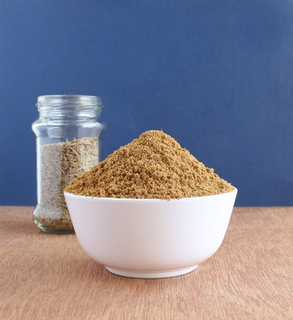 Healthy food cumin powder in a bowl and, in the background, a glass bottle with cumin seeds.