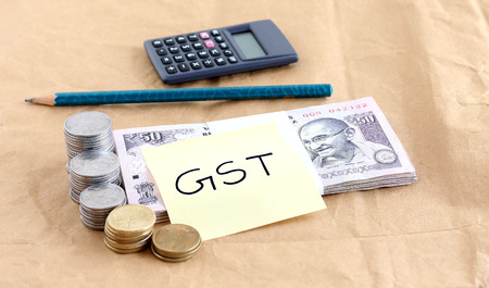GST or goods and services tax concept, highlighted with a bundle of  Indian rupees and stacks of coins and handwritten text.の写真素材
