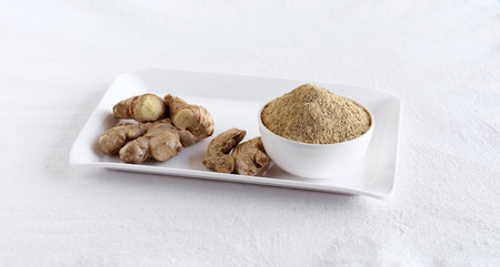 Ginger powder, a healthy food, in a bowl and raw and dried ginger on a tray.