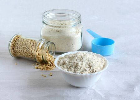 Sorghum flour, a healthy food and that is freshly ground, a whole grain and gluten free, in a ceramic bowl and jar, and sorghum spilled from a bottle, and a measuring cup.の写真素材