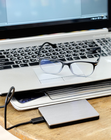 Notebook grey modern black keyboard with hdd grey and spectacles on wood tableの写真素材