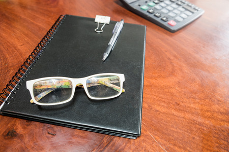 Eyeglasses with pen on book and culculator on wood tableの写真素材