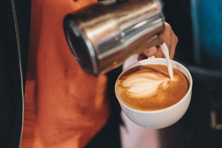 Barista pouring milk on coffee cup making heart shapeの写真素材