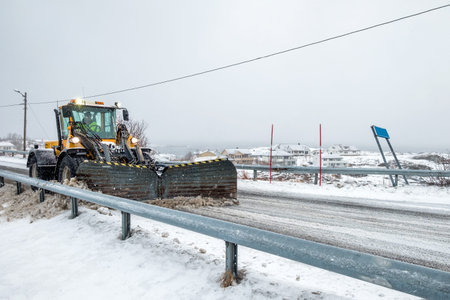 Yellow snowplough plowing on snowy road and blizzard