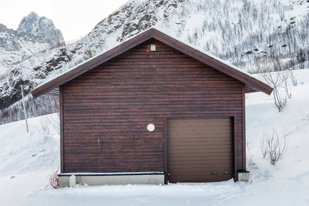 Wooden brown warehouse with roll door on snow hillの写真素材