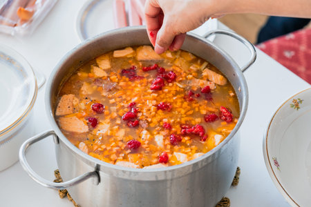 Hand pouring raspberry into Salmon soup with carrot and vegetables in stainless pot of traditional...