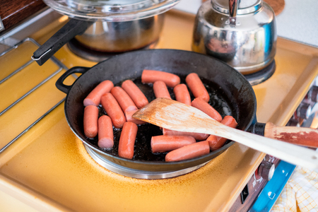 Cooking breakfast with sausages in frying skillet with wooden flipperの写真素材
