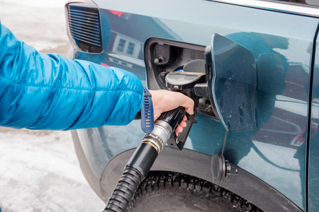 Hand hold refueling nozzle self-service in fuel tank at fuel station in winterの写真素材