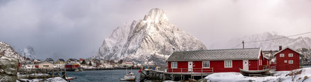 Panorama of Red house snowy with snow mountain on harbor at arctic coastline. Reine, Lofoten, Norway