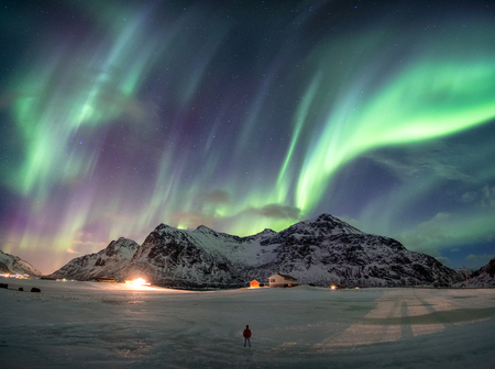 Fantastic Aurora borealis over snowy mountain with man standing at Skagsanden beach, Lofoten, Norwayの写真素材