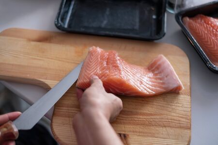 Hand chef using knife slice raw salmon on chopping blockの写真素材