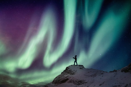 Man climber standing on snowy peak with aurora borealis and starry in the night skyの写真素材