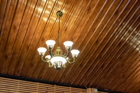 Retro chandelier lamp illuminate hanging on ceiling in wooden roomの写真素材