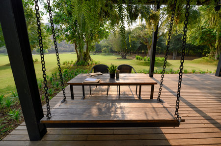 Wooden swing and chair in dining table with green flora on patio at sunset
