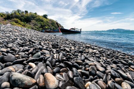 Black stone island with wooden boat on coastline in tropical sea at Koh Hin Ngamの写真素材
