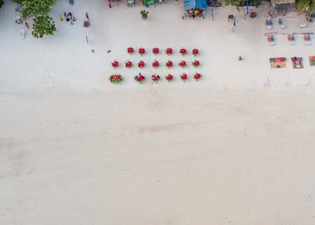 Top view of red tables and green chairs on the white beach at restaurant of resort