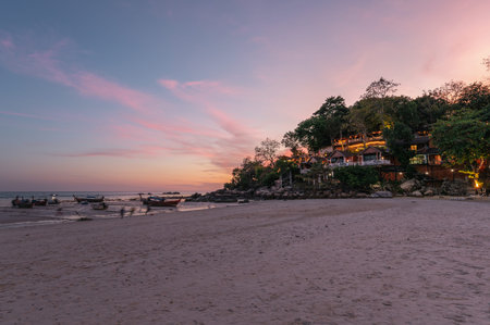 Seascape of wooden boat on the beach with resort on hill at evening